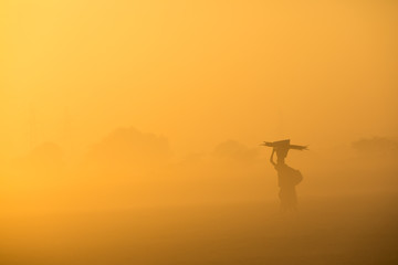 Fototapeta na wymiar silhouette of a woman in the sunrise carrying load