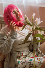 Smiling girl in a pink wig talking on a retro phone.