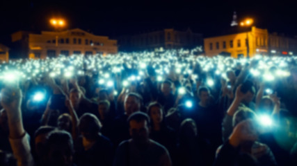 blurred silhouettes of a crowd of people at a live concert with mobile phone flashlights