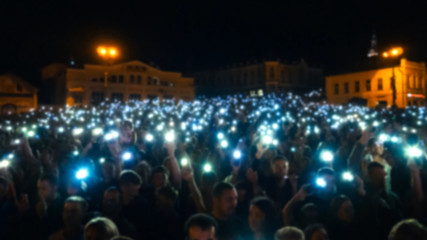 blurred silhouettes of a crowd of people at a live concert with mobile phone flashlights