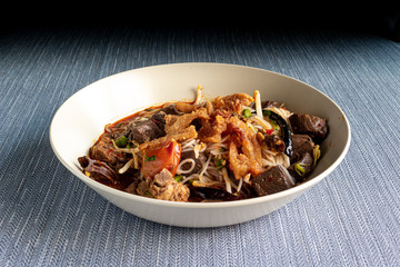 Burmese noodles with meat, liver, fried pork, tomato, mushroom, chili and other vegetables served on a plate