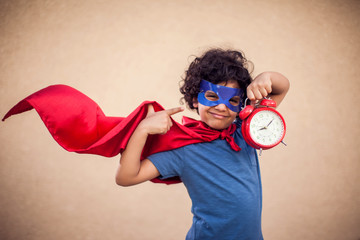 A portrait of kid boy in costume of superhero holdind alarm clock. Childhood, success and time...