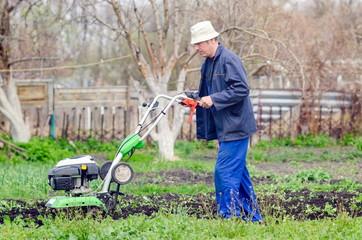 A man plows the land with a cultivator in a spring garden