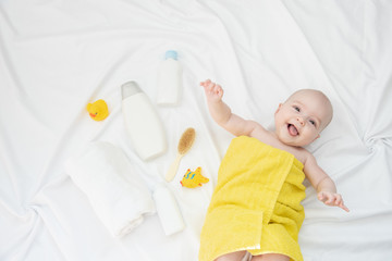 Portrait of a beautiful cheerful baby in a yellow towel after bath on a white cloth
