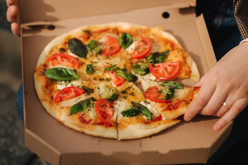 Close up of woman hold slice of vegan pizza in hand. Woman take pizza from pizza box. Vegetarian pizza with fresh tomatoes, balis and broccoli