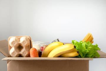 Box filled with food on an isolated background. In the box are vegetables, fruits, bananas, carrots, eggs, fresh salad, spaghetti, canned foods. Concept of donation, home delivery food.