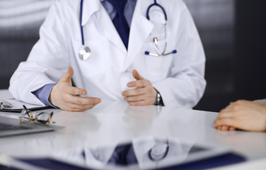 Unknown male doctor and patient woman discussing something while sitting in clinic and using clipboard. Best medical service in hospital, medicine, pandemic stop