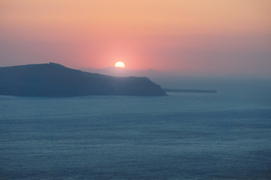 Sundown behind the islands with purple red lights over the ocean at the cliffs of Fira, Santorini, Greece