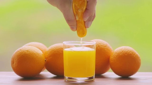 Cinemagraph, person hand squeezing out fresh juice from orange fruit into glass, outdoors at terrace 