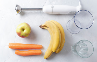 Submersible blender, a glass, an apple, bananas and carrots on a white background. Flat lay useful ingredients for making a fresh smoothie.