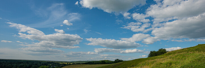 Fototapeta na wymiar Sky and clouds over a meadow on a hillside on a sunny day.