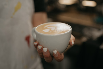 A female barista holds a cup of hot latte in her hand in a cafe. A waitress preparing a customer order.