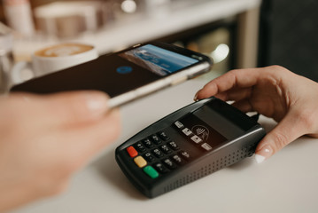 A lady paying for her latte with a smartphone by contactless NFC technology in a cafe. A female barista holds out a terminal for paying to a client in a coffee shop.