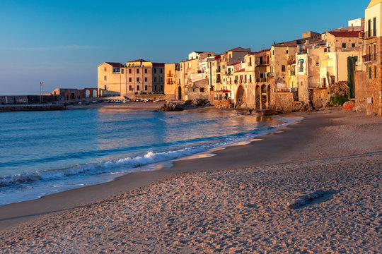 Beautiful view of empty sunny sand beach and old town of coastal city Cefalu at sunset, Sicily, Italy