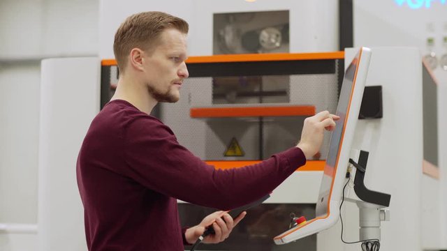 Side view waist up shot of focused middle aged engineer using touchscreen of vertical cnc milling machine in factory laboratory