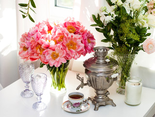 Still life with old russian samovar, rustic cup of tea, bouquet with peony flowers, glasses and candles.