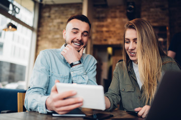Cheerful modern man and woman watching tablet in cafe