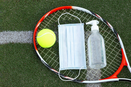 tennis racket , ball, medicine mask and sanitizer on green grass kort