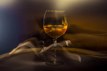 White wine in a glass on the table on a creative black background. Cigarette smoke in the bar and an alcoholic drink at a party or disco. Shooting in the dark key. Copy space.