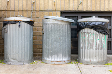 Three Metal Trash Cans Outside in front of a Brick Residential Building in Astoria Queens New York © James