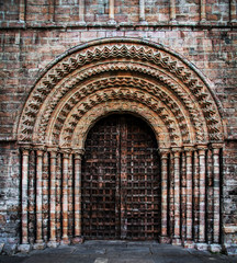 A large, ornate church doorway made from heavy wood with large arches and pillars supporting the rough and textured brickwork
