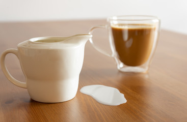 A jug and a glass of coffee with spilled milk