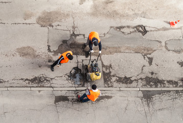 Road workers in orange vests repair the road. Pit removal and patching. View from above. works of...