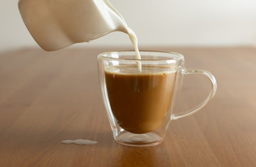 A glass of coffee with milk and pouring milk