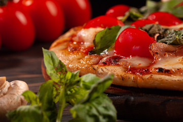 Homemade pizza with bacon and mushrooms on a wooden board. Tomatoes and basil.