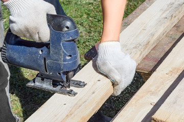 A male carpenter works with an electric jigsaw, sawing a tree.