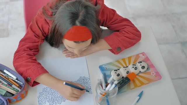 vista desde arriba de ni&ntilde;a de melena larga pintando filigranas en mesa de dibujo