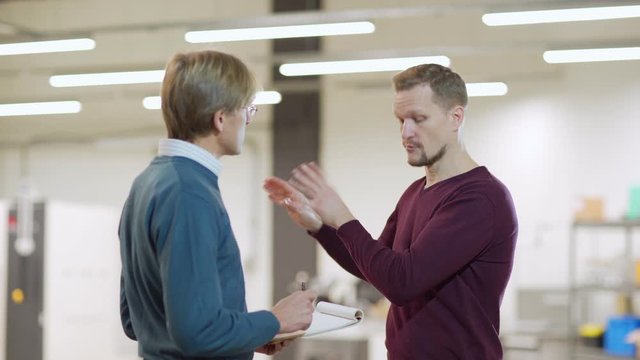Emotional middle aged engineer explaining his innovative idea to colleague and making sketch in his notebook in laboratory