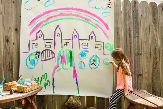 A young girl painting a castle on a large piece of paper outside in the backyard. 