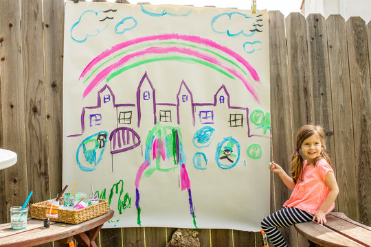 A young girl painting a castle on a large piece of paper outside in the backyard. 
