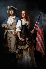 Man in form of officer of United States War of Independence and girl in historical dress of 18th century. July 4 is US Independence Day. Studio photo on black background