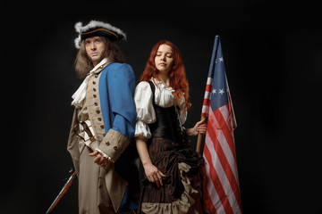 Man in form of officer of United States War of Independence and girl in historical dress of 18th century. July 4 is US Independence Day. Studio photo on black background