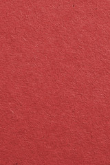 Fototapeta premium The surface of dark red cardboard. Rough paper texture with cellulose fibers. Saturated color. Vertical background or wallpaper. Top view from above. Macro