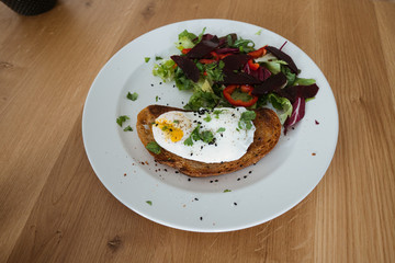 Poached egg on a piece of bread with green salad on a plate and on the wooden table. Healthy Breakfast