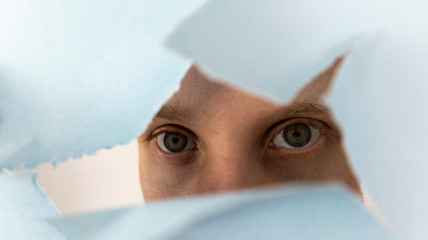 the man's eyes look through a torn sheet of paper