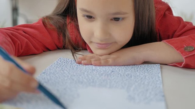 pequeña niña dibujando garabatos en papel con la cabeza apoyada en la mesa