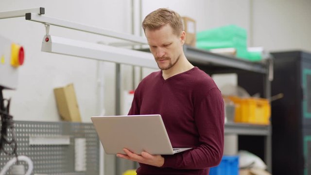 Tracking medium shot of middle aged engineer working on laptop computer standing by cnc machine in factory laboratory