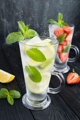 Infused or detox water with strawberry,lemon and  mint  in the two glasses  on the dark  background. Closeup. Location vertical.