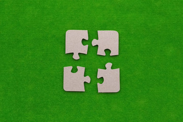 The four pieces of the puzzles out of cardboard on a green background. Interaction, making up of parts of the whole.