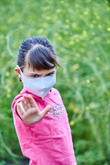 Niña con mascarilla en un ambiente ajardinado, con la palma extendida en señal de stop.