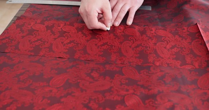 4K Close up on hands of a tailor working in his shop, drawing template on paisley lining fabric. tailor is drawing lines on a fabric with his chalk in order to make a suit-flat profile