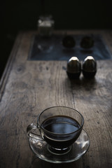 a dark Cup of coffee against a dark table and a pepper pot with a salt shaker