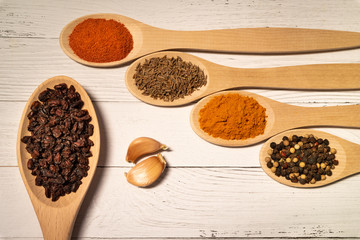 Seasonings for cooking pilaf: garlic, barberry, cumin, saffron, red and black pepper in wooden spoons on the table.