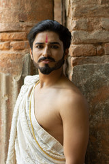 Portrait of an Indian pujari/ worshiper in bare body Indian ethnic traditional wear standing in front of a old temple wall. Indian lifestyle and ethnic wear.