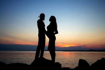 Silhouette of a couple expecting a baby. Married couple by the sea on a sunset background.