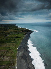the black sand beach and coastal waves of the sea, the ocean and green rice fields